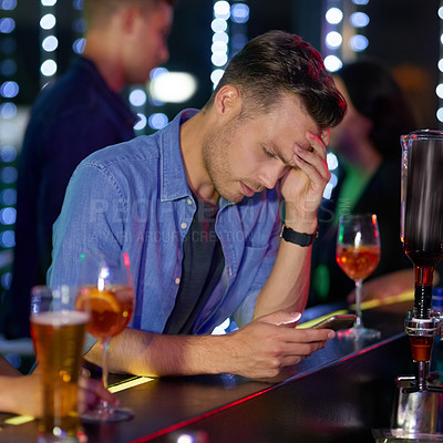 Buy stock photo Shot of an upset looking young man reading a text on his cellphone while sitting at the counter of a nightclub