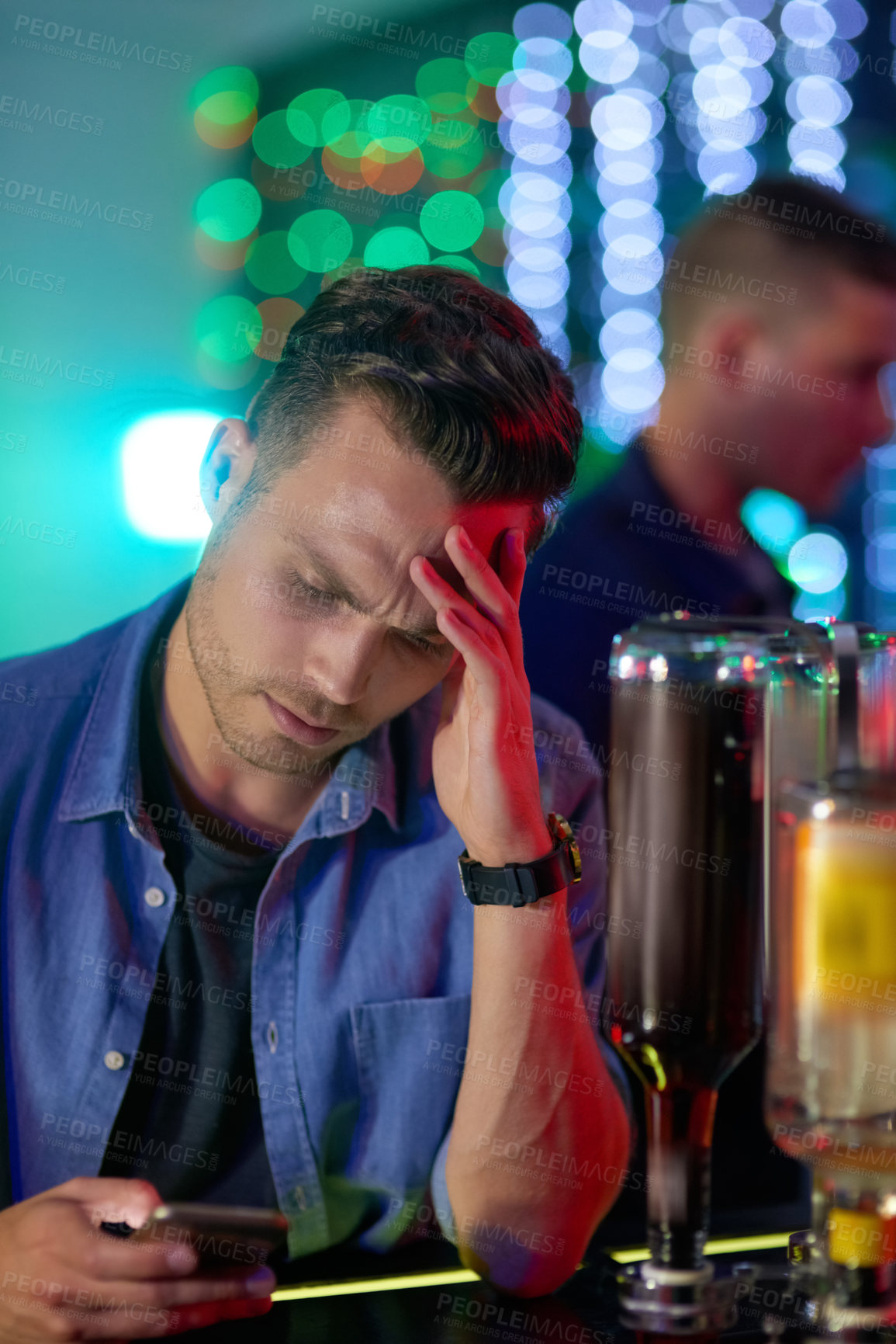 Buy stock photo Shot of an upset looking young man reading a text on his cellphone while sitting at the counter of a nightclub