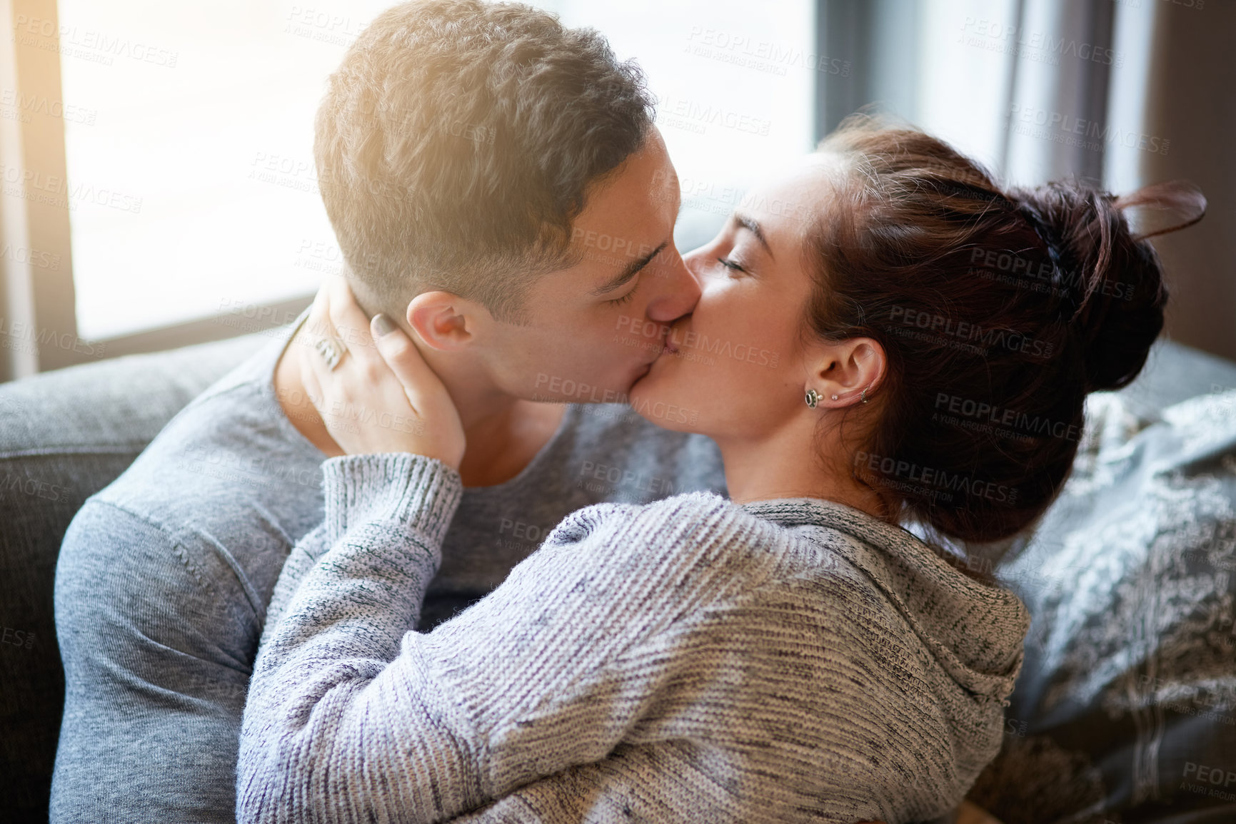 Buy stock photo Shot of an affectionate young couple kissing on the sofa at home