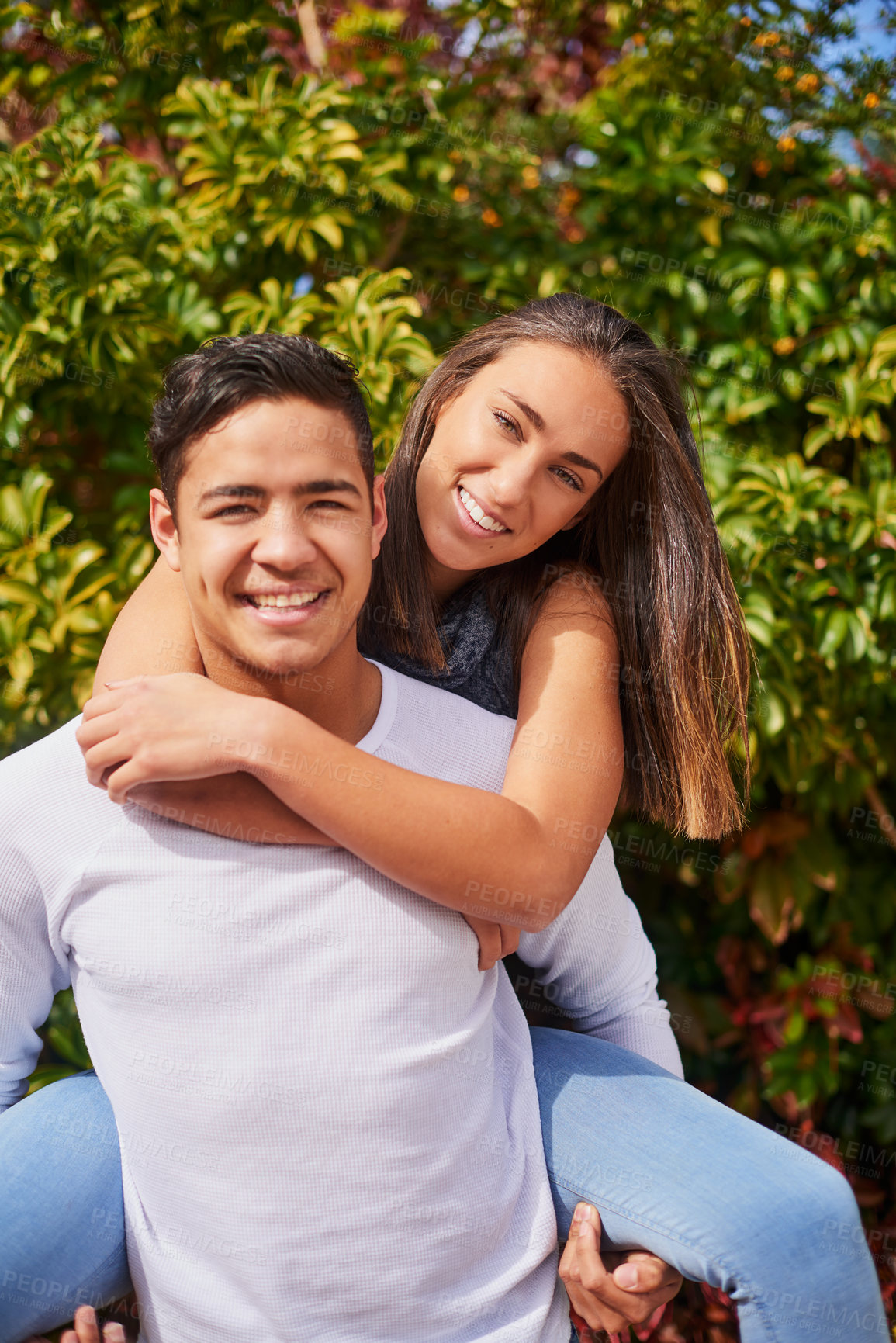 Buy stock photo Portrait of a smiling young man giving his girlfriend a piggyback outside