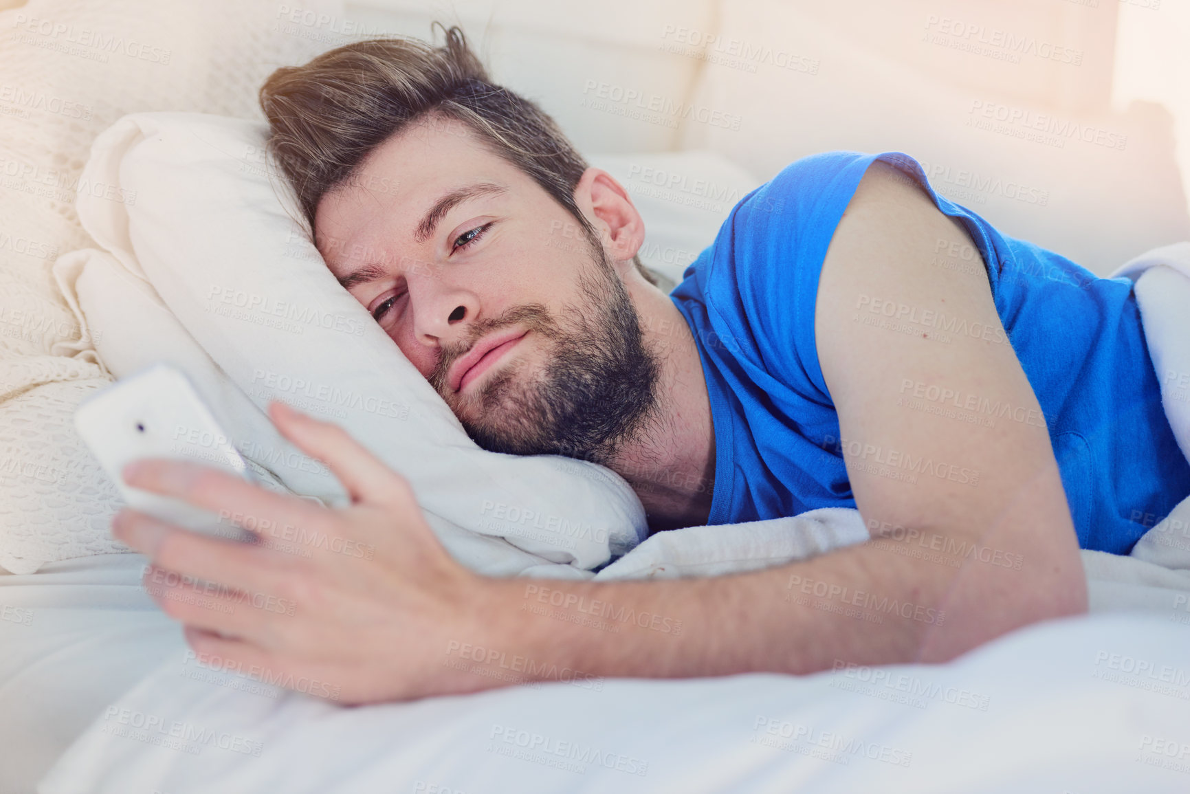 Buy stock photo Cropped shot of a handsome young man texting on his cellphone while lying in bed at home