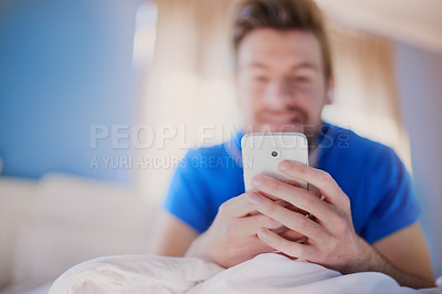 Buy stock photo Cropped shot of a young man texting on his cellphone while lying on his bed