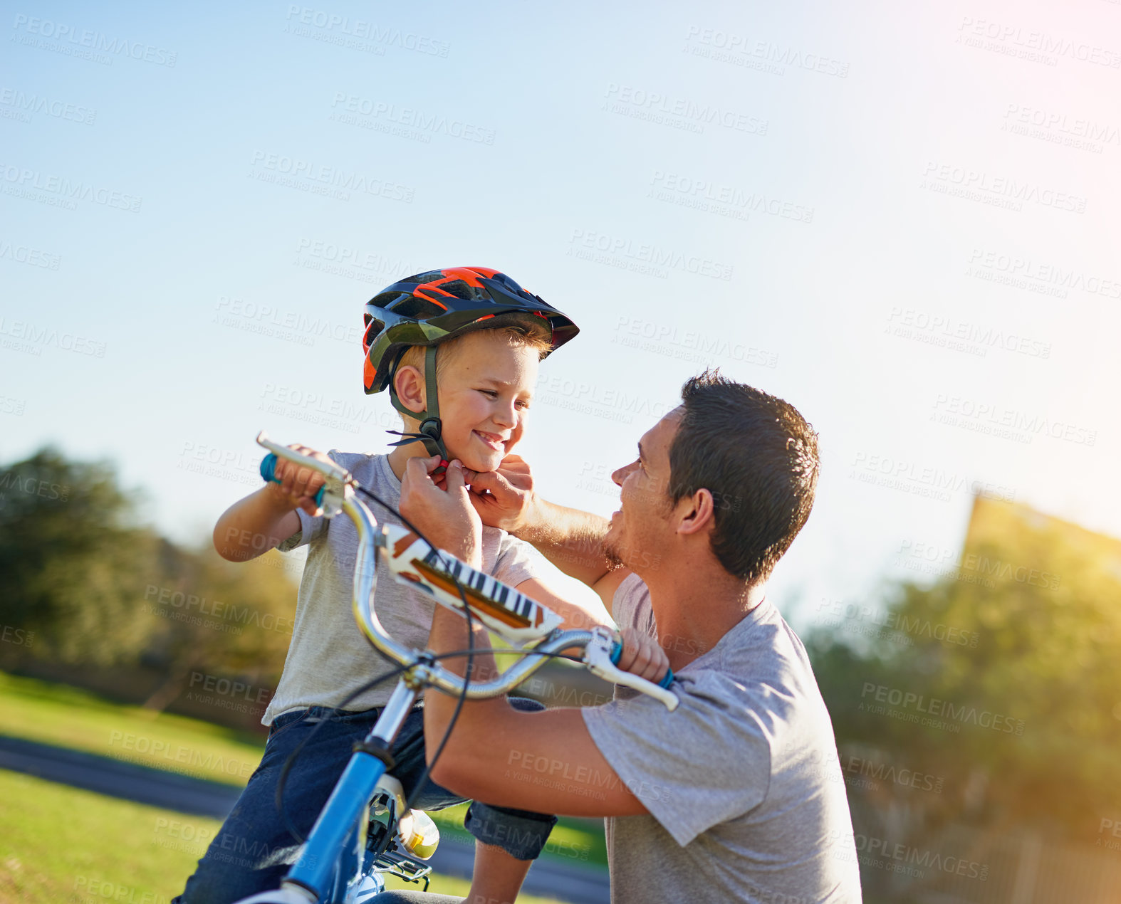 Buy stock photo Shot of a father putting a helmet on his son while teaching him how to ride a bicycle in the park
