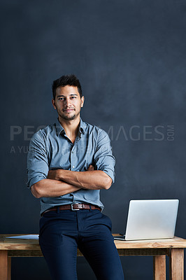 Buy stock photo Portrait of a handsome young businessman standing in front of a desk against a dark background