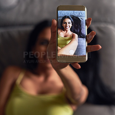 Buy stock photo High angle shot of an attractive young woman taking a selfie while lying on her sofa at home