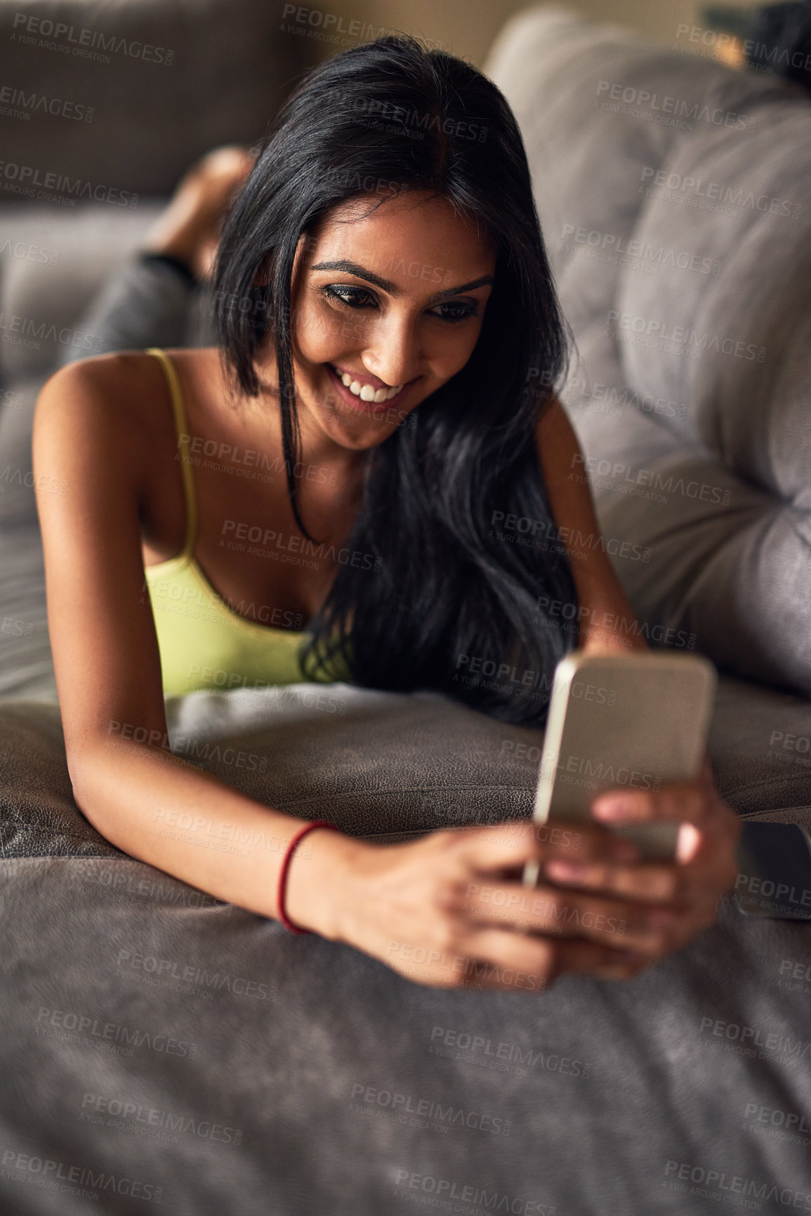 Buy stock photo Shot of an attractive young woman sending a text messahe while lying on her sofa at home