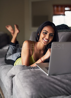 Buy stock photo Shot of an attractive young woman surfing the net while lying on her sofa at home