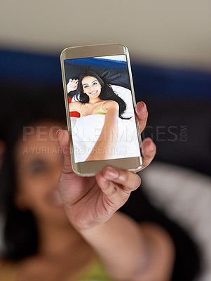 Buy stock photo Cropped shot of a happy young woman relaxing in bed and using her phone to take a selfie