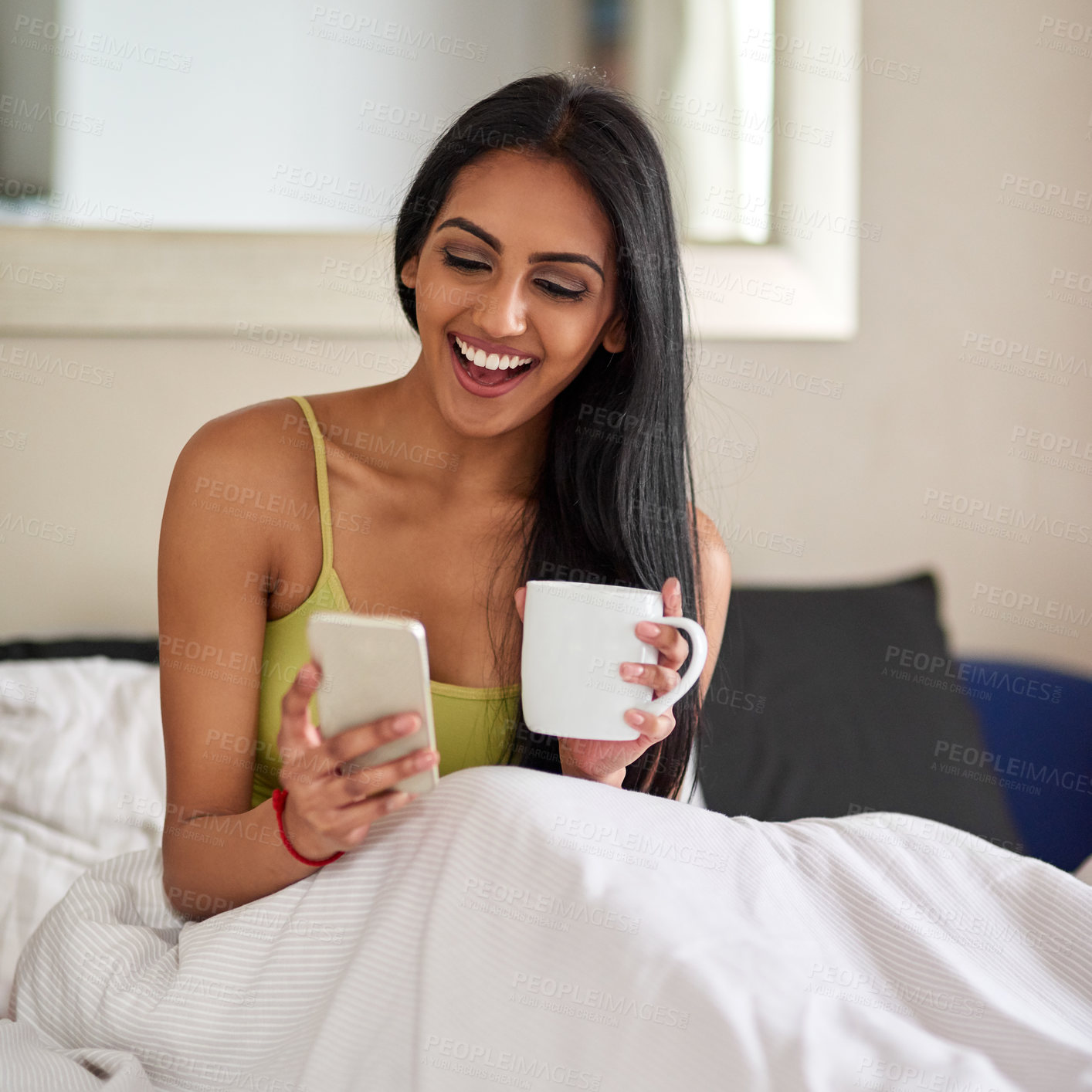 Buy stock photo Shot of a relaxed young woman drinking coffee and using her phone in bed