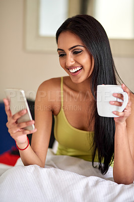 Buy stock photo Shot of a relaxed young woman drinking coffee and using her phone in bed