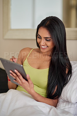 Buy stock photo Shot of a relaxed young woman using a digital tablet in bed