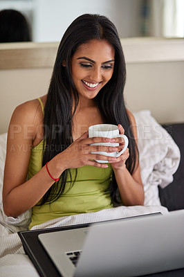 Buy stock photo Shot of a relaxed young woman using a laptop and drinking coffee in bed
