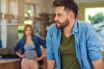 Buy stock photo Shot of a young man looking upset after a fight with his wife who is standing in the background
