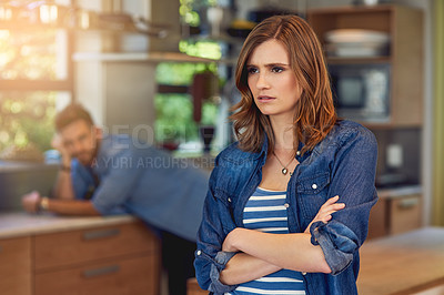 Buy stock photo Shot of a young woman looking upset after a fight with her husband who is standing in the background