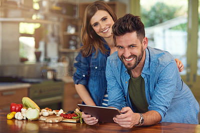 Buy stock photo Portrait of a happy young couple using a digital tablet while preparing a healthy meal together at home