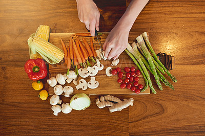 Buy stock photo High angle shot of a woman cutting a variety of healthy vegetables on a chopping board