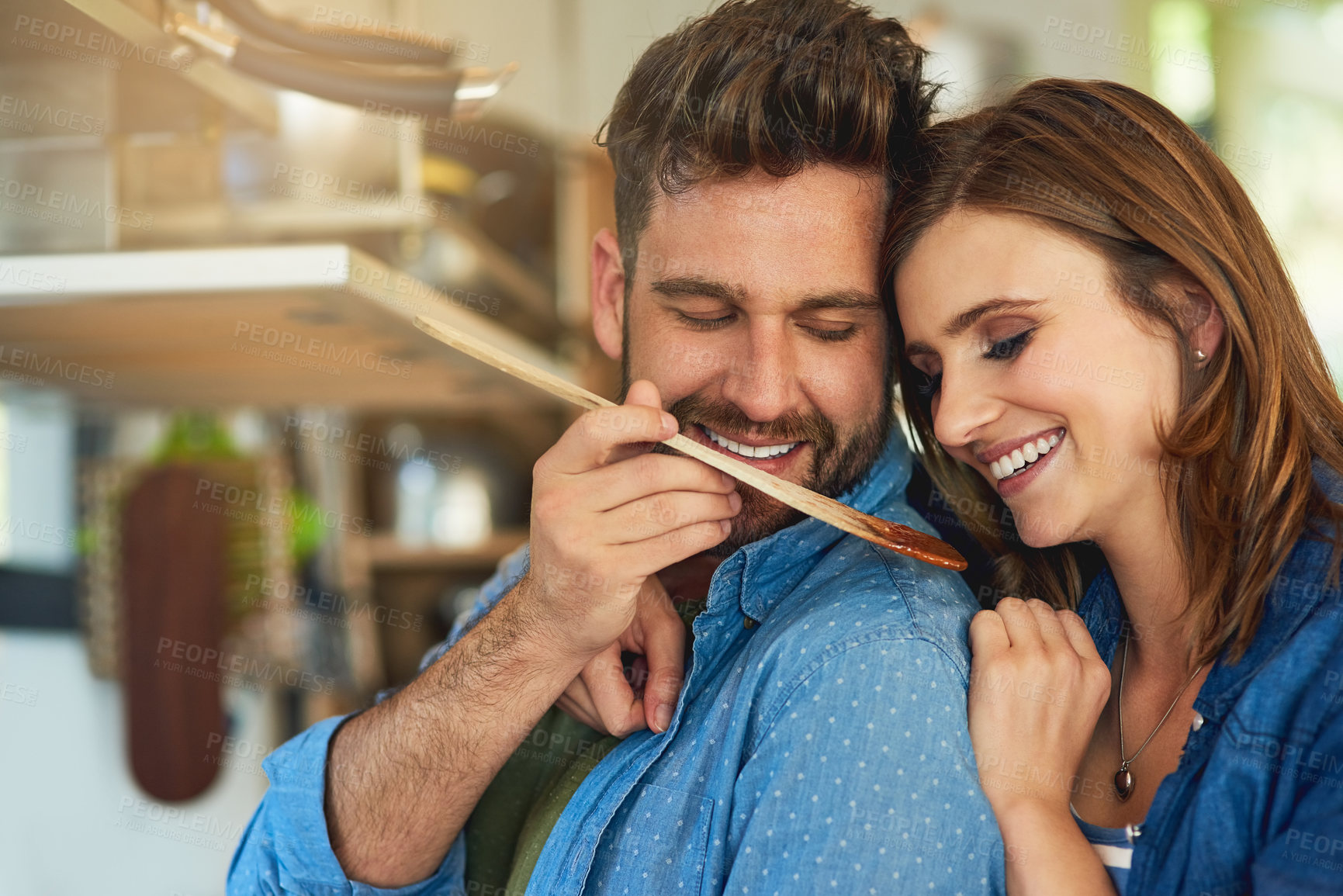 Buy stock photo Shot of a man giving his wife a taste of the food that he’s preparing at home