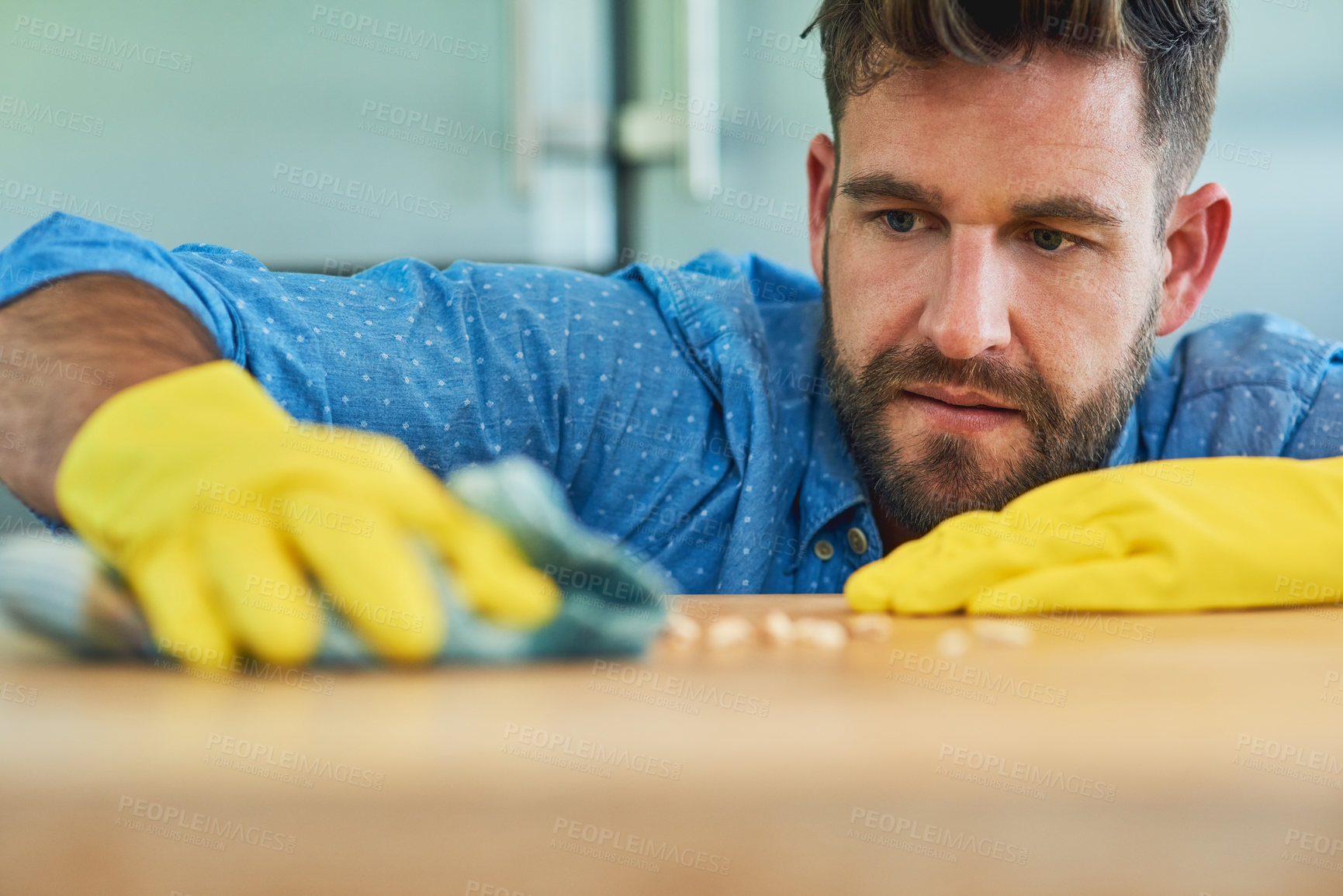 Buy stock photo Shot of a man wearing rubber gloves while wiping a table at home