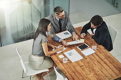 Buy stock photo Shot of three colleagues sitting around a meeting tablet in the office
