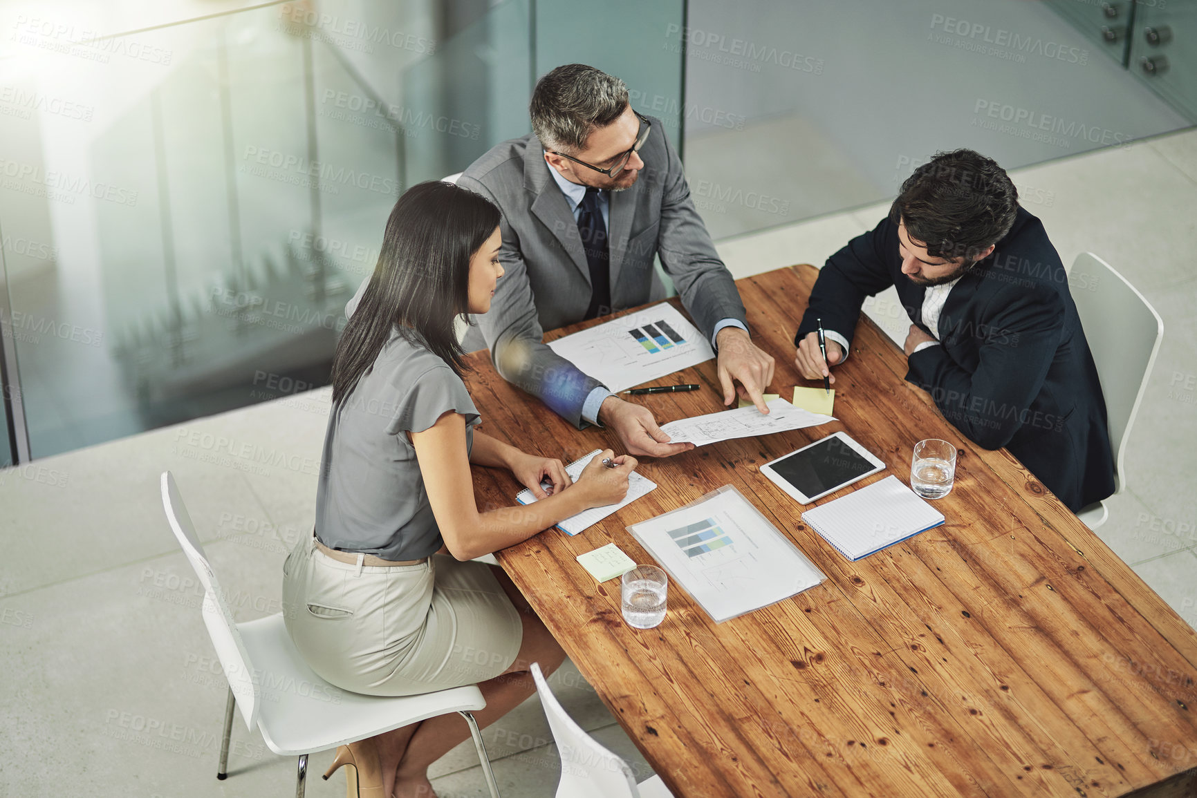 Buy stock photo Shot of three colleagues sitting around a meeting tablet in the office