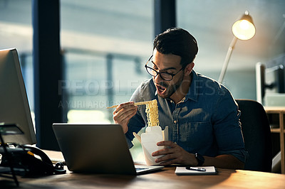 Buy stock photo Young businessman working late and eating at desk. Man having takeout food in the office at work station in the evening. Male worker feeding his brain from work during the night at the workplace.