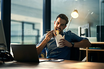 Buy stock photo Young hungry businessman working late and eating at desk. Man having takeout food in the office at work station in the evening. Male entrepreneur eating asian meal during the night at the workplace