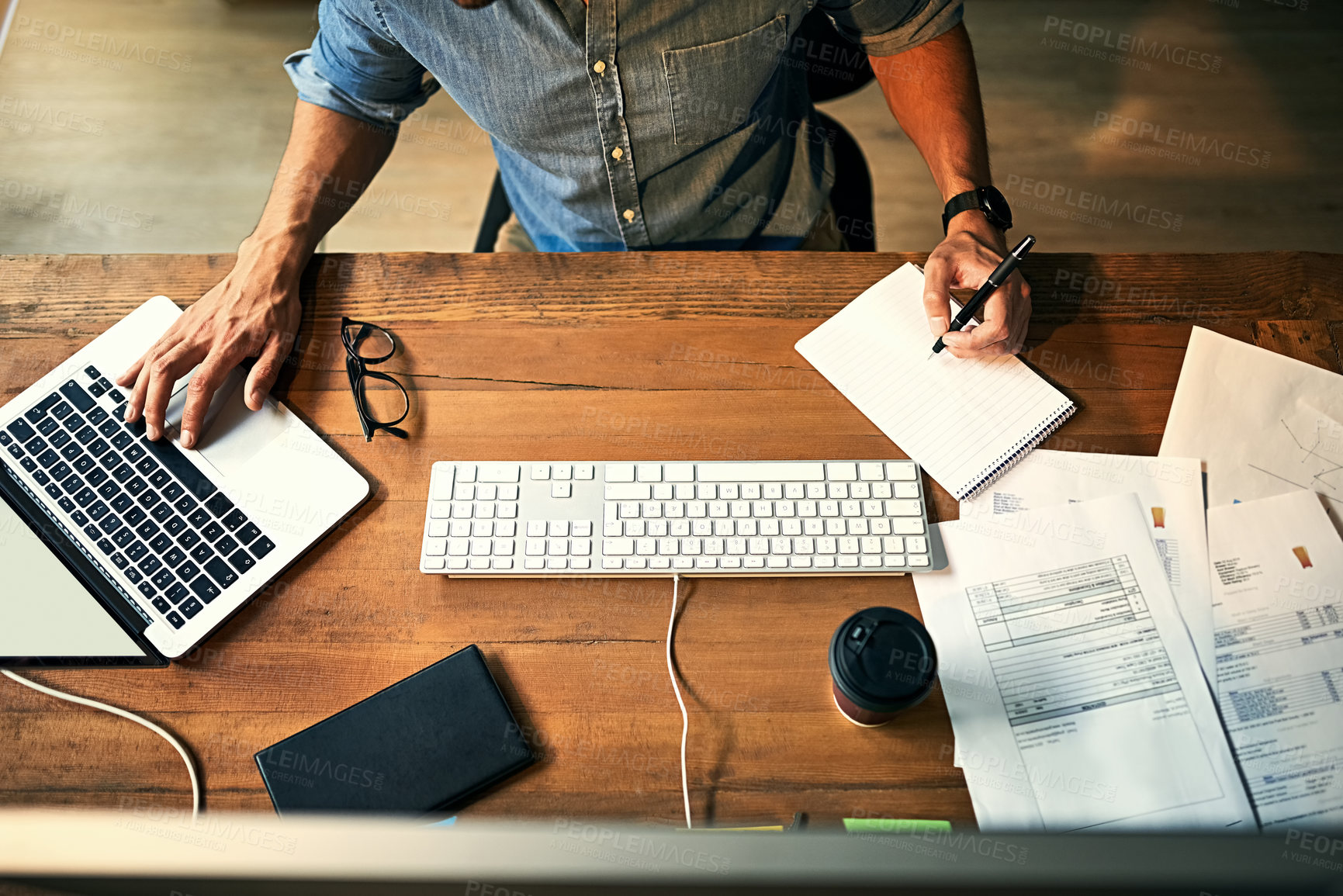 Buy stock photo High angle shot of a businessman using a computer and writing notes during a late night at work