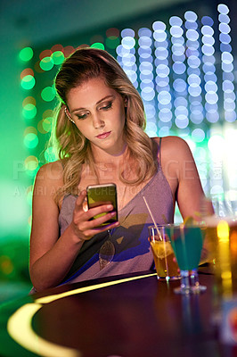 Buy stock photo Shot of young woman using her cellphone while sitting alone in a nightclub