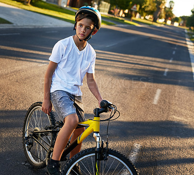 Buy stock photo Shot of a young boy riding his bicycle through his neighbourhood