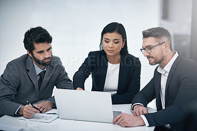 Buy stock photo Shot of three businesspeople gathered around a laptop in the boardroom