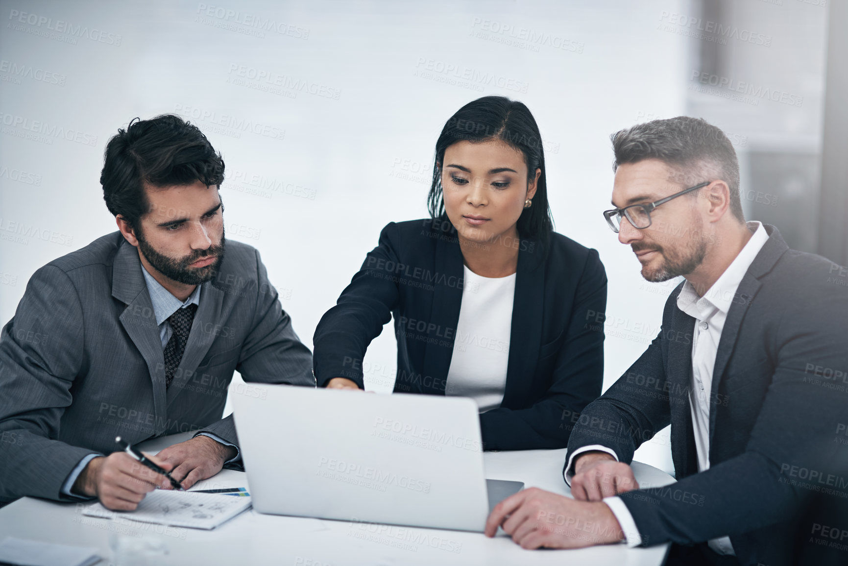 Buy stock photo Shot of three businesspeople gathered around a laptop in the boardroom