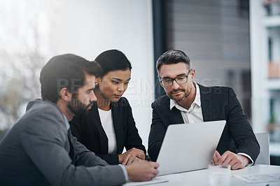 Buy stock photo Shot of three businesspeople gathered around a laptop in the boardroom