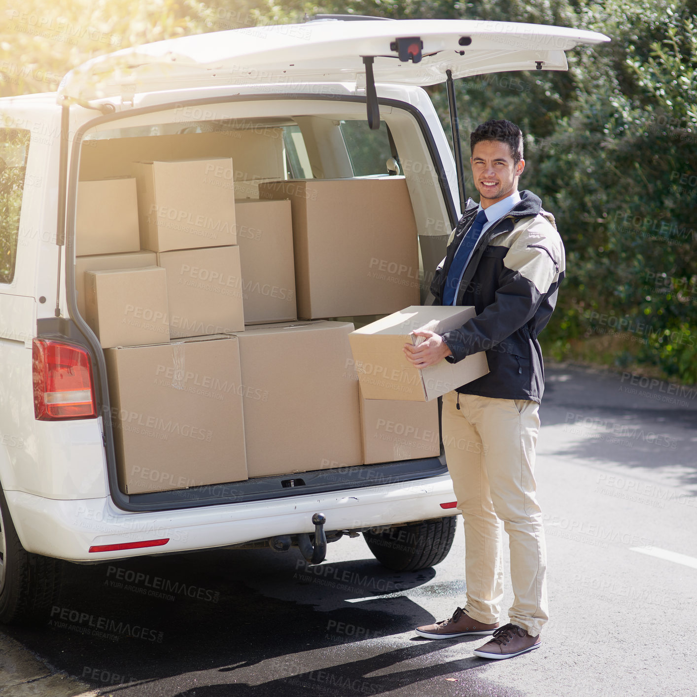 Buy stock photo Portrait of a friendly delivery man unloading cardboard boxes from his van