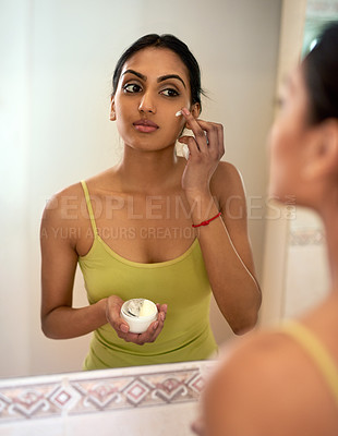 Buy stock photo Cropped shot of a young woman applying moisturiser to her face in the bathroom