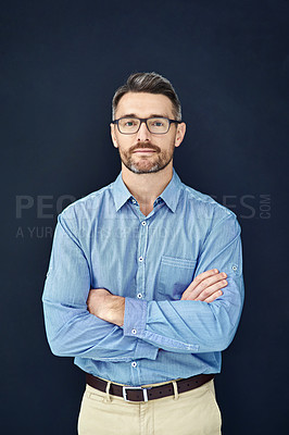 Buy stock photo Studio portrait of a handsome businessman standing with his arms folded against a dark background