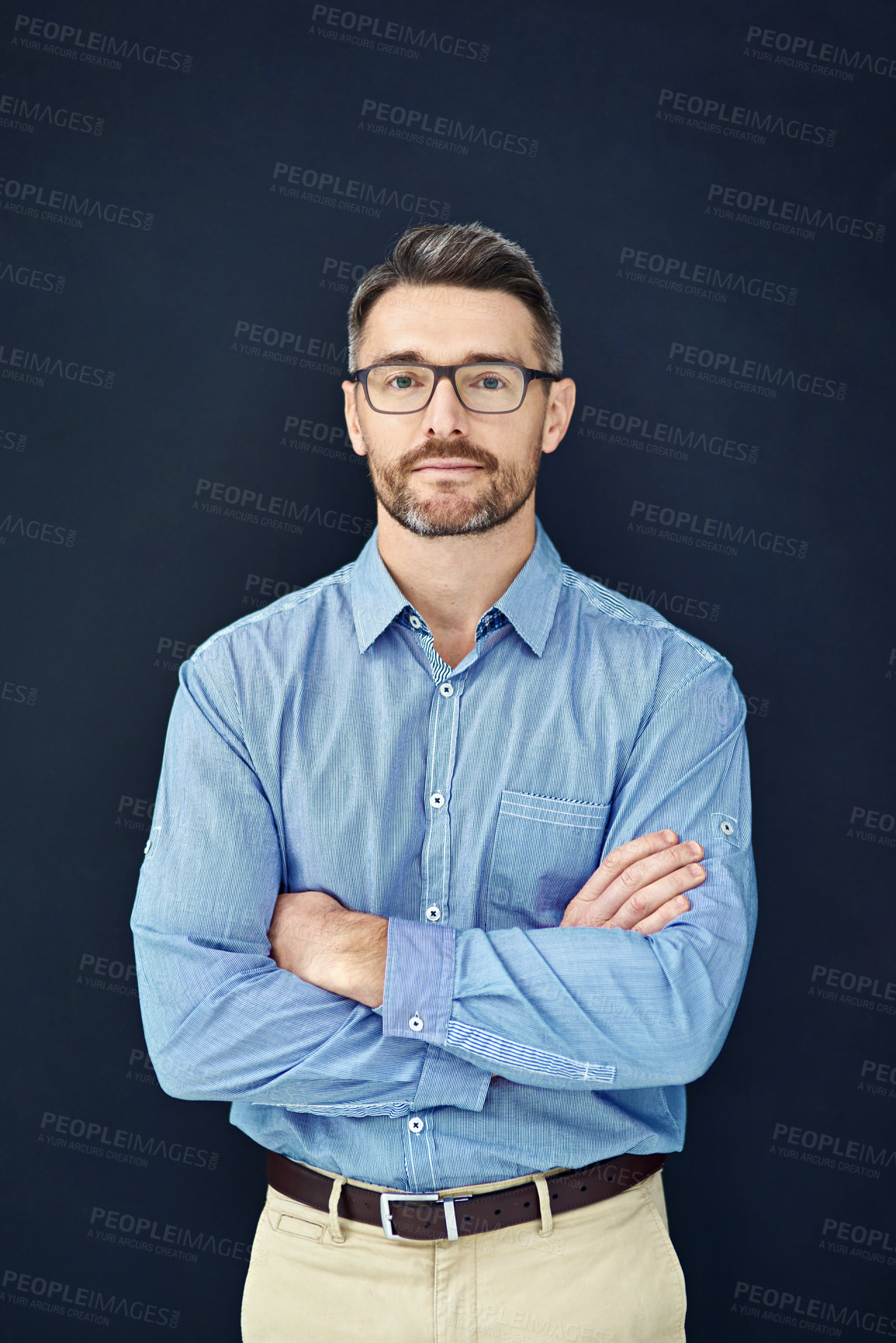 Buy stock photo Studio portrait of a handsome businessman standing with his arms folded against a dark background