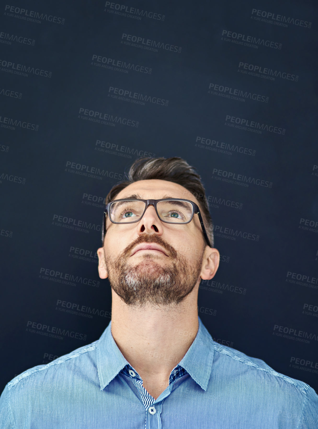 Buy stock photo Studio portrait of a handsome businessman looking upward while standing against a dark background