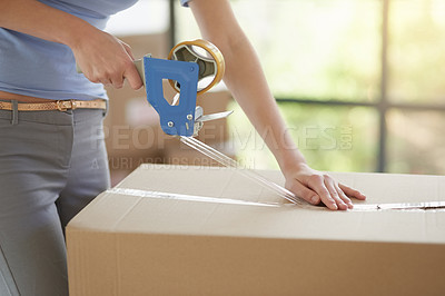 Buy stock photo Shot of an unidentifiable young woman closing a cardboard box with tape at home