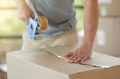 Buy stock photo Shot of an unidentifiable young man closing a cardboard box with tape at home