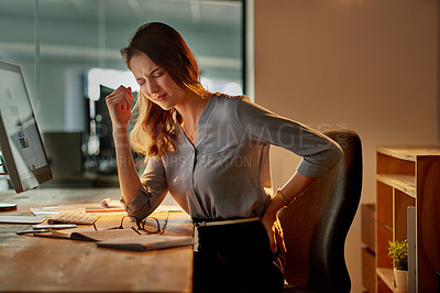 Buy stock photo Shot of an attractive young businesswoman holding her back in pain while working late in the office