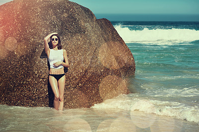 Buy stock photo Shot of a beautiful young woman posing against a beach rock