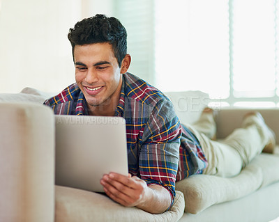 Buy stock photo Shot of a handsome young man using his laptop while relaxing on the sofa at home