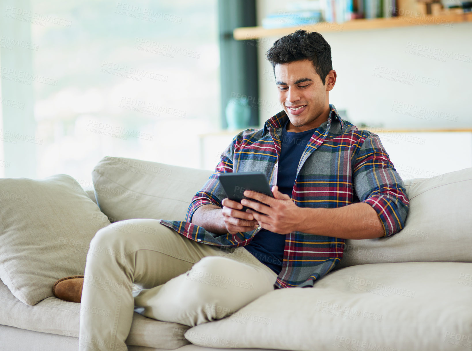 Buy stock photo Shot of a handsome young man using his tablet while relaxing on the sofa at home