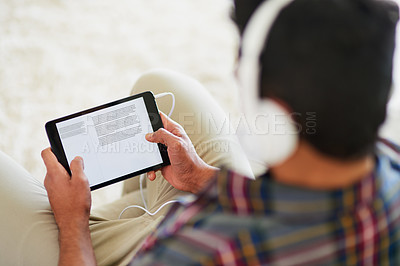 Buy stock photo Shot of a young man listening to music on his tablet while relaxing on the sofa at home