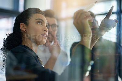 Buy stock photo Shot of a group of colleagues brainstorming together on a glass wall in an office