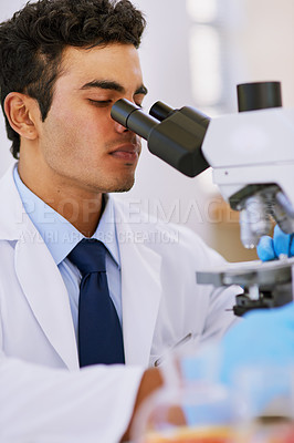 Buy stock photo Shot of a lab technician using a microscope while sitting in a lab