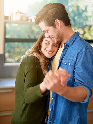 Buy stock photo Shot of an affectionate young couple dancing hand in hand together in their kitchen