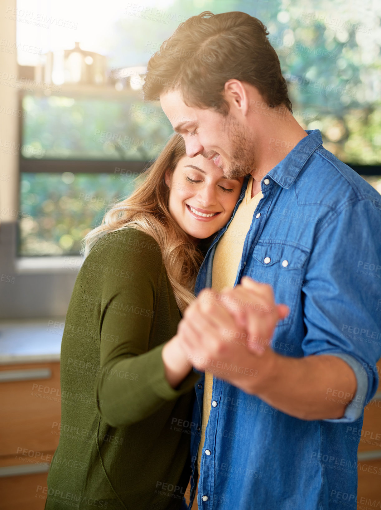 Buy stock photo Shot of an affectionate young couple dancing hand in hand together in their kitchen