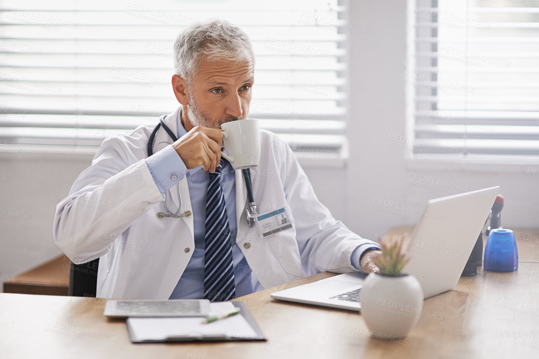 Buy stock photo Shot of a mature male doctor using a laptop at his desk