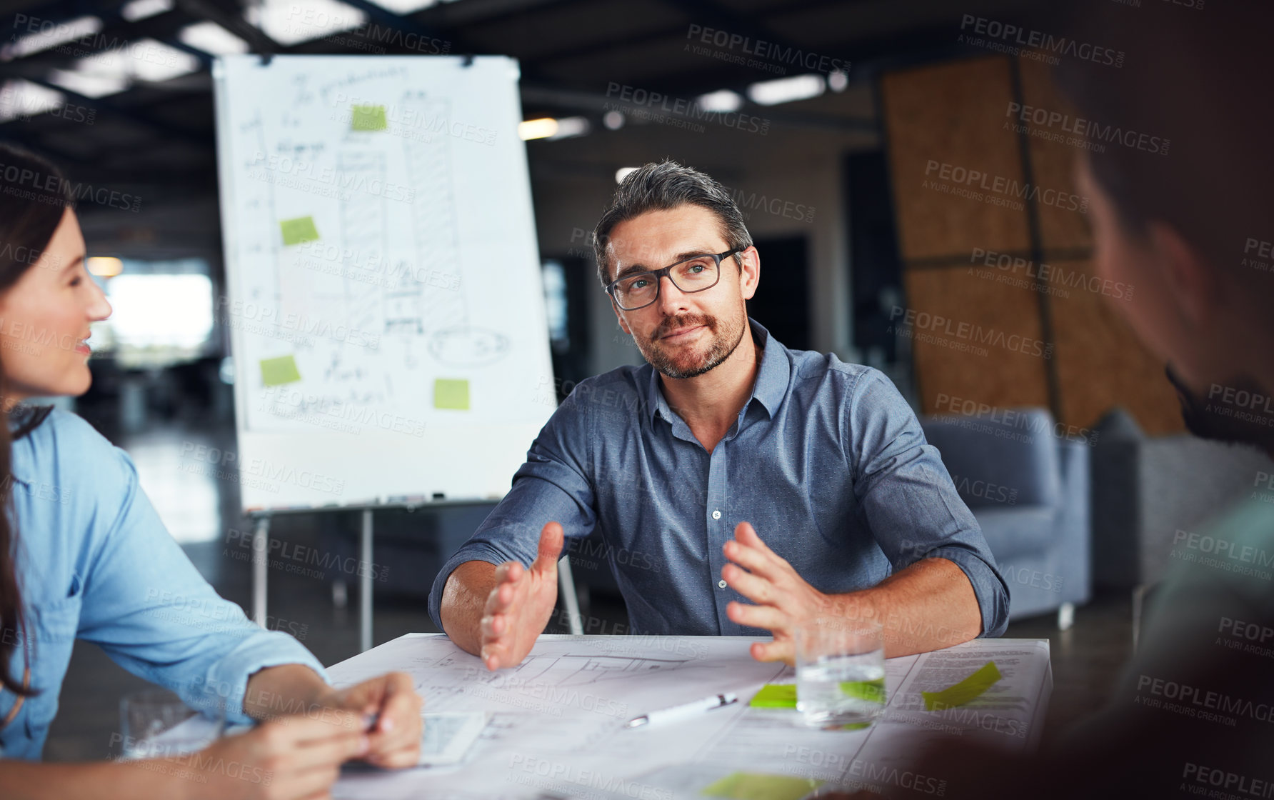 Buy stock photo Shot of a mature manager talking to his team while sitting around a table in an office